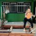 Fitness enthusiast practicing Pilates on a reformer machine in a modern, brightly lit studio.