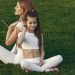 A mother and daughter in white activewear sitting on grass, enjoying a sunny day outdoors.