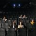 Image of diverse audience sparsely seated in a dimly lit cinema hall.